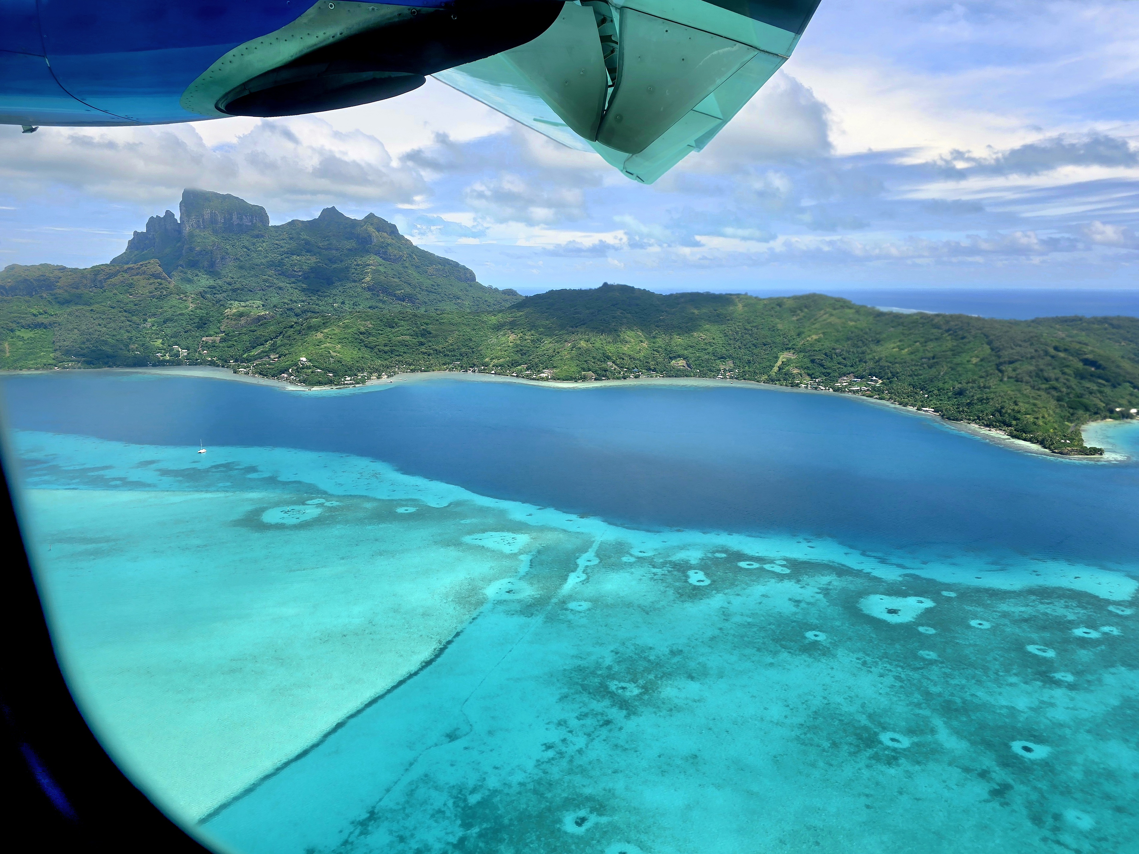 Thatched Polynesian fare roofs with Mount Otemanu and forested peaks under a blue sky.
